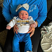 Macie joined the competition — help win amazing prizes! baby, infant, child, person, blue_clothing, hat, bow, adult_hands, sitting, couch, blanket, indoor, portrait, cute, wide_eyes, supporting_hands, cozy, casual, clothing, fabric