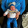 baby, infant, child, person, blue_clothing, hat, bow, adult_hands, sitting, couch, blanket, indoor, portrait, cute, wide_eyes, supporting_hands, cozy, casual, clothing, fabric