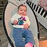 baby, infant, child, smile, sweater, hair_clip, baby_rocker, indoor, flooring, furniture, crib, blanket, pink, blue_pants, cute, cheeks, happy, person, clothing, home