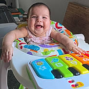 Sophia Grace Leon is registered to the contest to win money with this photo: baby, baby_walker, toy_piano, colorful, smiling, happy, infant, indoor, child, playtime, musical_toy, seat, foot, arms, face, clothing, furniture, joy, expression, home