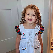 Gianna is registered to the contest to win money with this photo: child, girl, curly_hair, smiling, white_dress, barefoot, indoor, wooden_floor, colorful_sleeves, embroidery, parrot, happy, portrait, standing, person, floor, home, cute, young, clothing