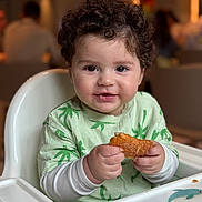 Assil a rejoint le concours — aidez-le/la à gagner de superbes lots ! toddler, child, high_chair, food, pastry, curly_hair, green_shirt, indoor, smile, happy, face, hand, cute, baby, dolphin, table, feeding, person, young_child, seated