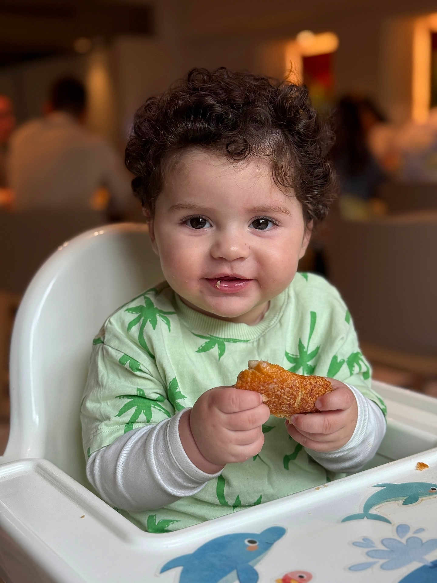 Assil a rejoint le concours — aidez-le/la à gagner de superbes lots ! toddler, child, high_chair, food, pastry, curly_hair, green_shirt, indoor, smile, happy, face, hand, cute, baby, dolphin, table, feeding, person, young_child, seated
