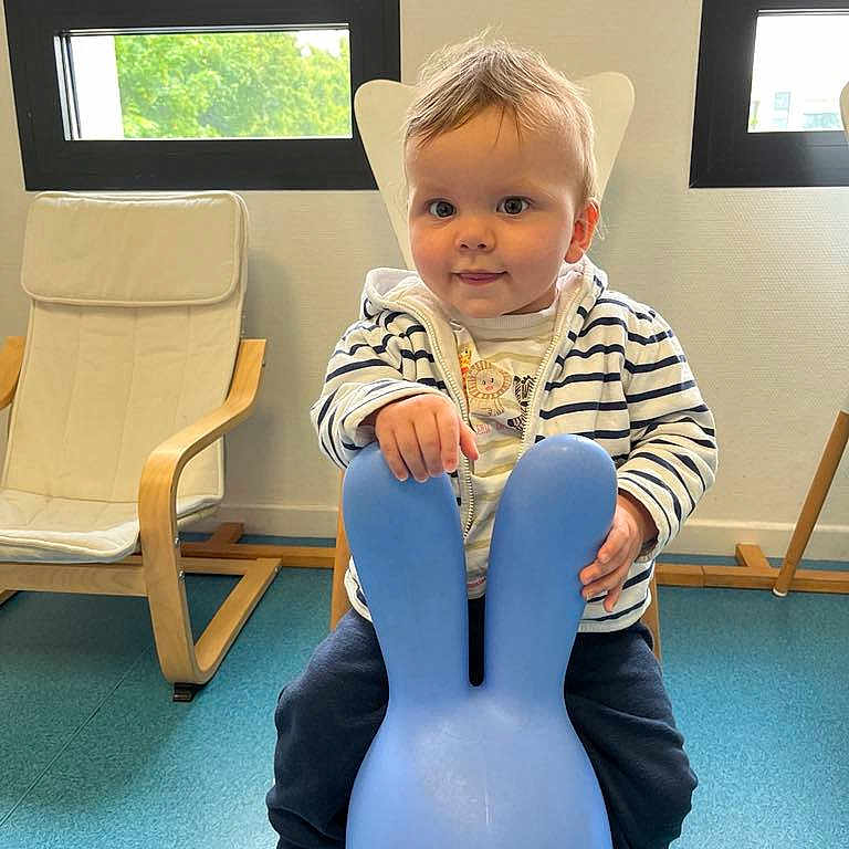 Raphaël participe au concours pour gagner de l'argent avec cette photo : blue, bunny, chair, child, cute, eyes, floor, hand, hoodie, indoor, natural_light, pants, person, play, sitting, smile, striped_clothing, toddler, toy, window
