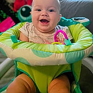 Kendra is registered to the contest to win money with this photo: baby, smiling, infant, child, baby_seat, toy, pink_toy, indoor, happy, cute, green, blue, clothing, face, person, sitting, chubby_legs, window, blurred_background, soft_lighting