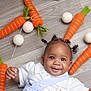 baby, child, smile, happy, floor, carrot, felt, toy, playful, cute, hair, pigtails, white_clothing, button, indoor, decoration, string, orange, green, round_object