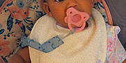 Kamrynn is registered to the contest to win money with this photo: toddler, pacifier, bib, braids, beads, child, high_chair, floral_cushion, indoor, cute, baby, portrait, infant, clothing, seat, face, person, young_child, adorable, closeup