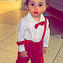 toddler, child, indoor, barefoot, red_pants, white_shirt, bow_tie, suspenders, floor, tiles, curious, standing, person, young_child, clothing, portrait, cute, baby, face, expression