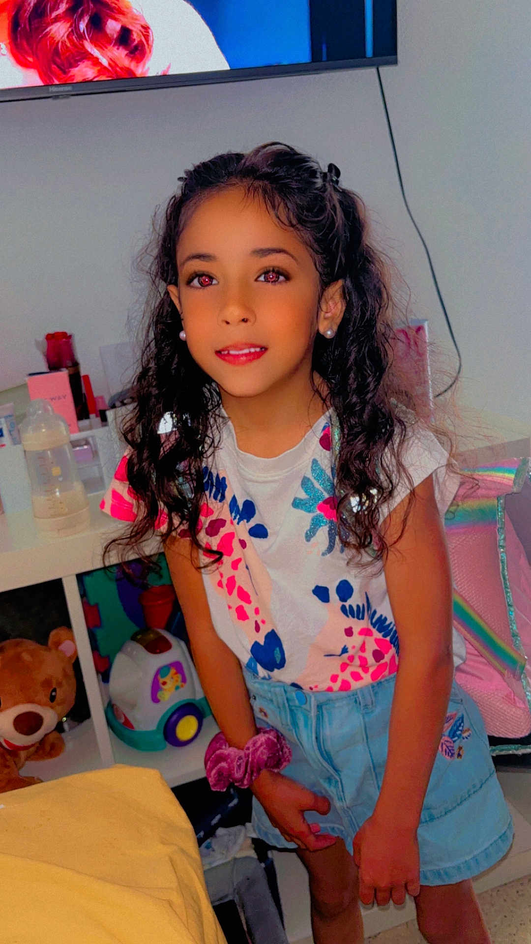 Djenna participe au concours pour gagner de l'argent avec cette photo : child, girl, smile, curly_hair, earrings, colorful_shirt, denim_skirt, toy, teddy_bear, room, indoor, furniture, bottle, playful, youth, person, portrait, casual_clothing, hair_accessory, childhood