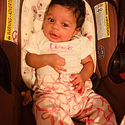 Olivia joined the competition — help win amazing prizes! baby, infant, child, cute, curly_hair, white_clothing, pink_clothing, baby_carrier, cushion, floral_pattern, warning_label, indoor, seated, portrait, looking_at_camera, hand, face, eyes, smile, comfortable