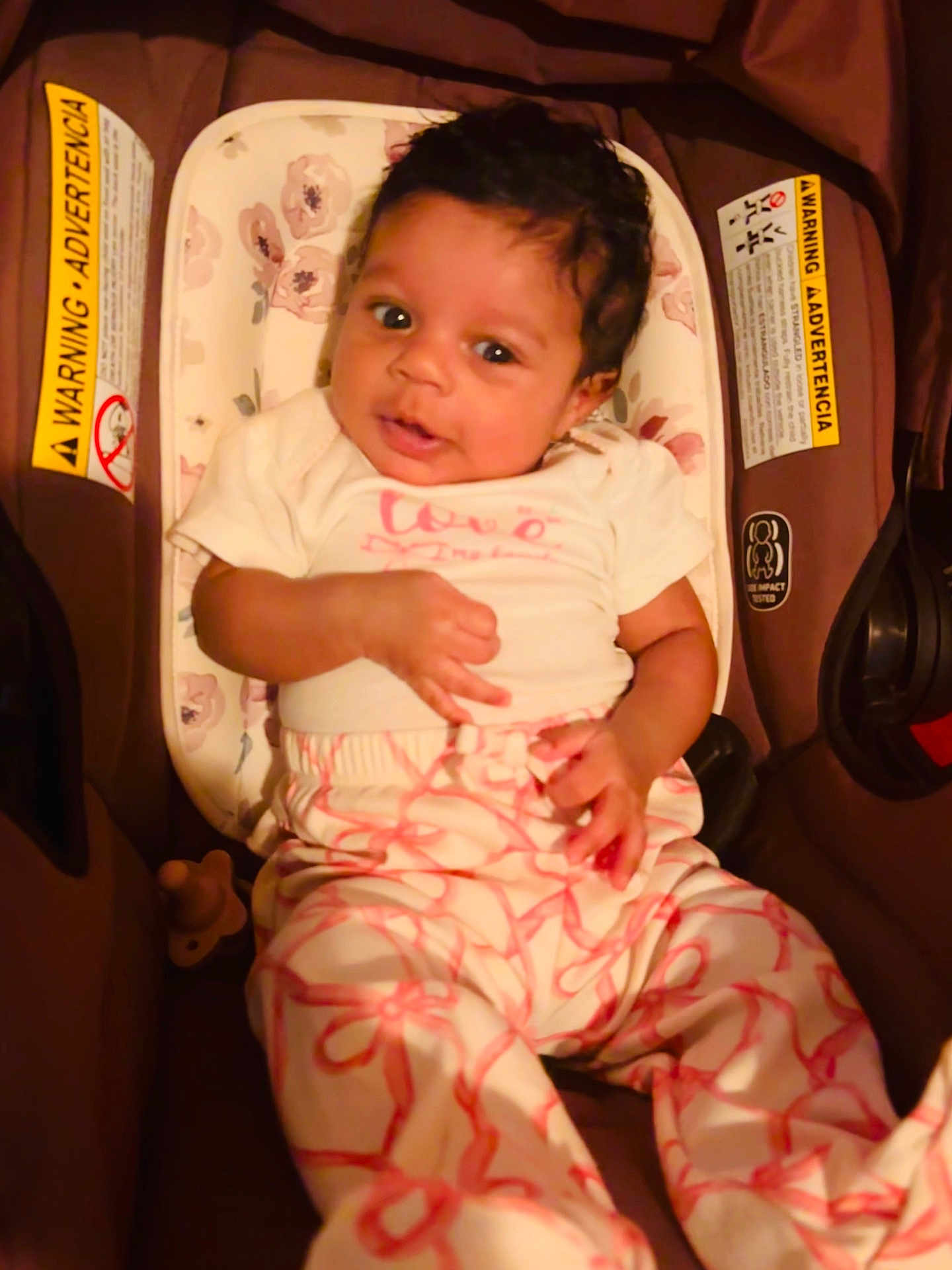 Olivia joined the competition — help win amazing prizes! baby, infant, child, cute, curly_hair, white_clothing, pink_clothing, baby_carrier, cushion, floral_pattern, warning_label, indoor, seated, portrait, looking_at_camera, hand, face, eyes, smile, comfortable