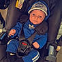 Lukas participe au concours pour gagner de l'argent avec cette photo : baby, car_seat, blue_clothing, cap, child, infant, black_car_seat, face, person, indoors, footwear, socks, straps, safety_harness, wood_floor, curious, wide_eyes, seated, casual_clothing, hat