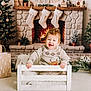 baby, carpet, child, christmas_tree, cozy, crate, decorations, festive, fireplace, fur, gifts, happy, holiday, indoor, potted_plants, reindeer, smile, stockings, sweater, wood