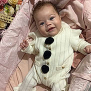 Adrianna is registered to the contest to win money with this photo: baby, infant, smiling, knitted_outfit, white_clothing, black_buttons, pink_blanket, pacifier, flower_bouquet, basket, soft_fabric, indoor, cute, happy, person, portrait, child, lying_down, cozy, warm