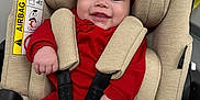 Adrianna is registered to the contest to win money with this photo: baby, infant, car_seat, red_clothing, red_headband, smiling, child, seat_belt, safety, cute, happy, indoors, person, face, small_hands, car_seat_padding, fabric, head_support, baby_clothes, toddler