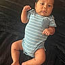 baby, infant, child, portrait, lying_down, striped_onesie, blue_clothing, blanket, fluffy_blanket, indoor, close_up, face, eyes_open, fist, arms, legs, bare_feet, serious_expression, soft_lighting, candid_photo