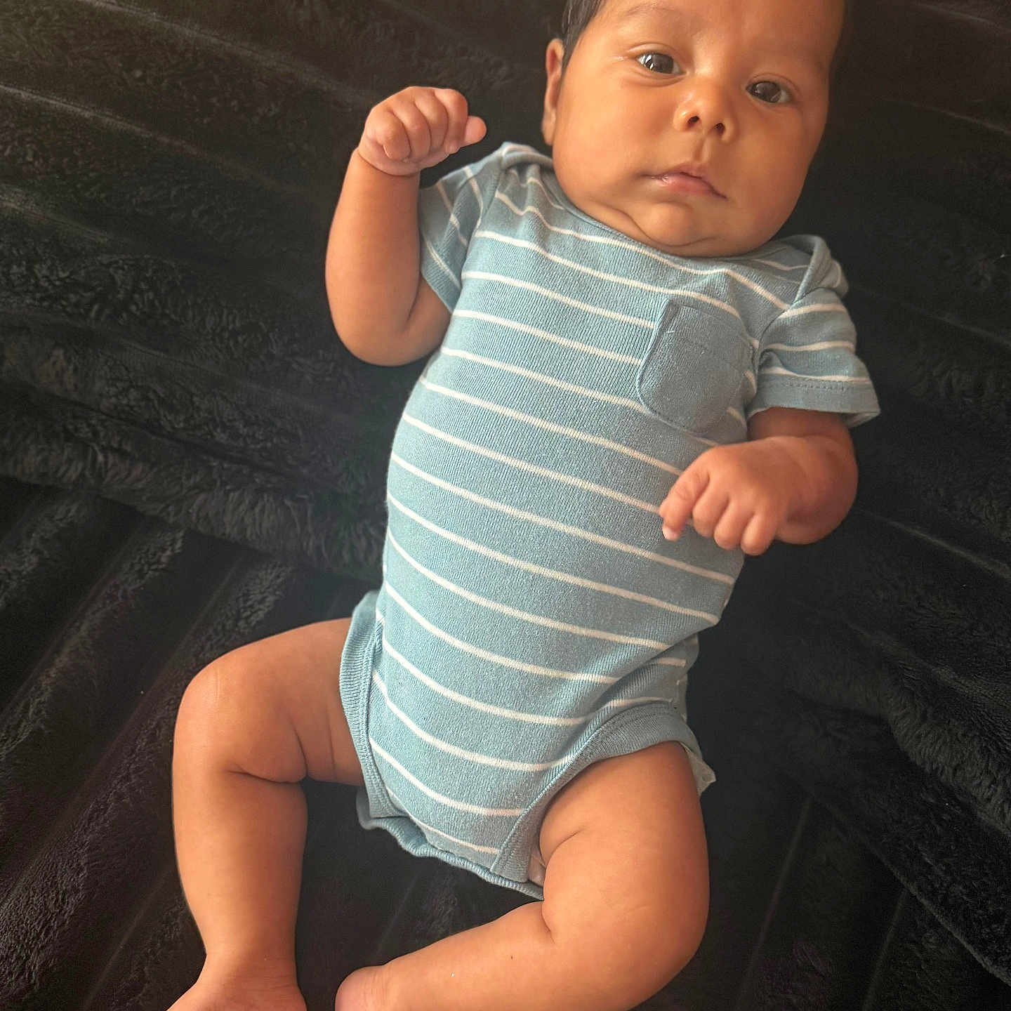 Thiago Marquez joined the competition — help win amazing prizes! baby, infant, child, portrait, lying_down, striped_onesie, blue_clothing, blanket, fluffy_blanket, indoor, close_up, face, eyes_open, fist, arms, legs, bare_feet, serious_expression, soft_lighting, candid_photo