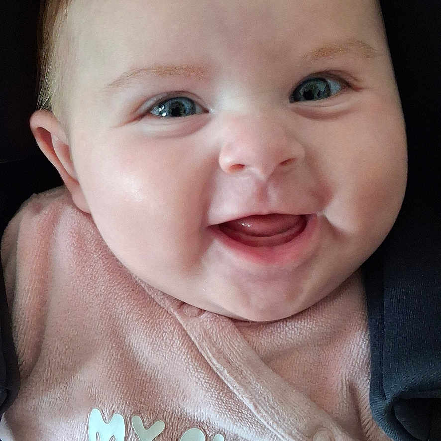 Nina participe au concours pour gagner de l'argent avec cette photo : apparel, baby, baby_girl, blue_eyes, car_seat, child, closeup, clothing, cute, face, happy, infant, person, pink_clothing, portrait, seatbelt, sitting, smiling, soft_texture, young