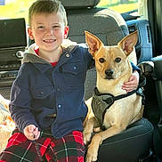Dash joined the competition — help win amazing prizes! boy, child, dog, pet, vehicle_interior, seat, harness, plaid_pants, jacket, smiling, arm_around, canine, friendship, indoors, casual_clothing, young, happy, sitting, leash, daylight