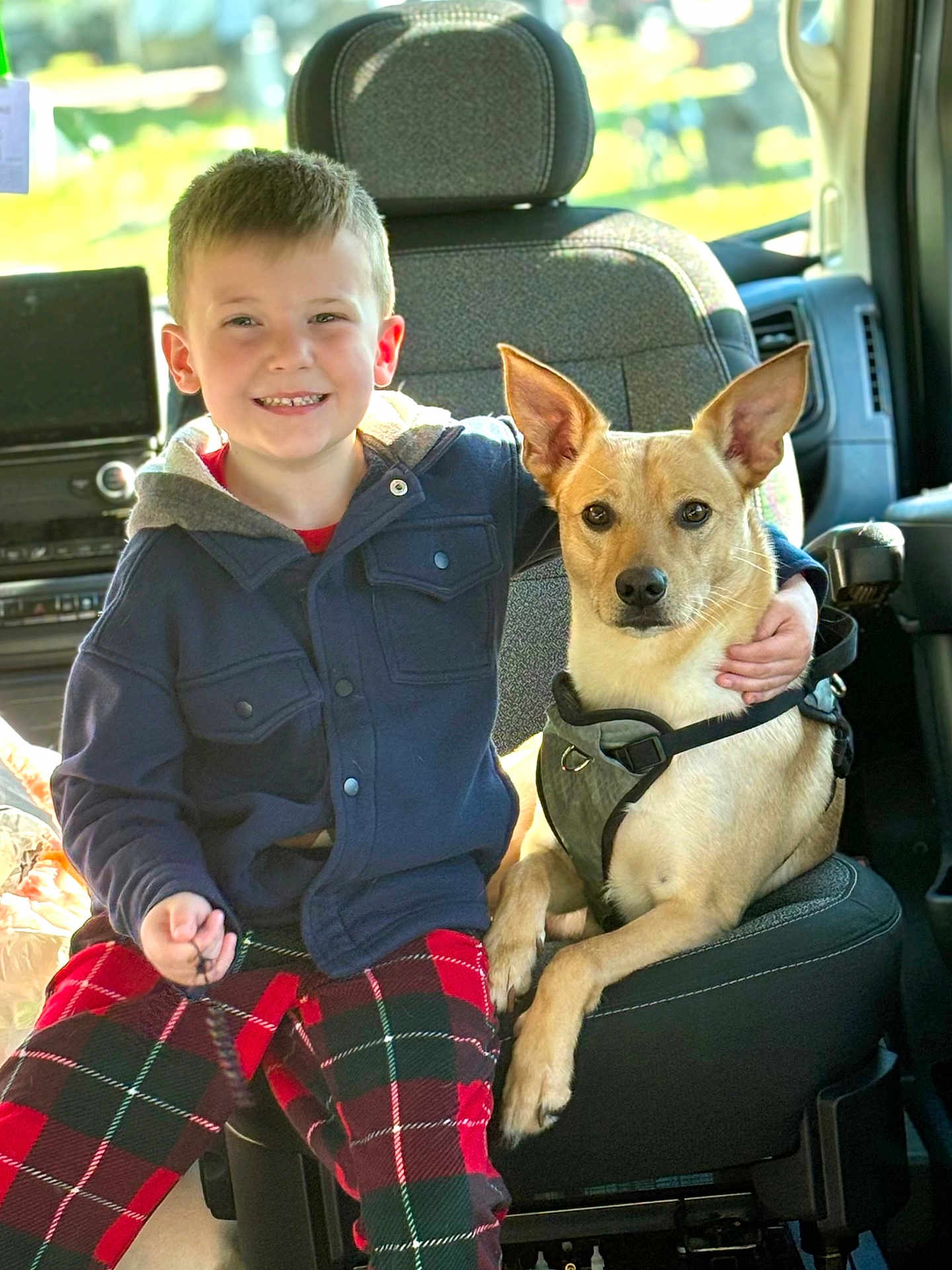 Dash joined the competition — help win amazing prizes! boy, child, dog, pet, vehicle_interior, seat, harness, plaid_pants, jacket, smiling, arm_around, canine, friendship, indoors, casual_clothing, young, happy, sitting, leash, daylight