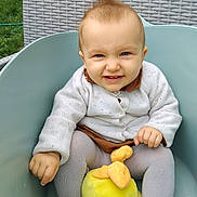 Mégara a rejoint le concours — aidez-le/la à gagner de superbes lots ! baby, blue_chair, child, clothing, cute, grass, grin, happy, knit_sweater, leggings, mohawk, outdoor, person, plush_toy, portrait, seated, smile, toddler, woven_chair, yellow_toy