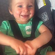 Liam is registered to the contest to win money with this photo: baby, child, smiling, car_seat, green_clothing, dinosaur_patch, straps, safety_harness, happy, cute, infant, person, seatbelt, indoors, hands, face, head, shoulder, legs, toddler