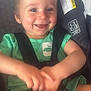 baby, child, smiling, car_seat, green_clothing, dinosaur_patch, straps, safety_harness, happy, cute, infant, person, seatbelt, indoors, hands, face, head, shoulder, legs, toddler