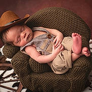 Houston joined the competition — help win amazing prizes! baby, newborn, sleeping, cowboy_hat, hat, overalls, knit_chair, crocheted_chair, props, little_feet, portrait, studio, cozy, brown, wooden_wheel, cowhide_rug, hands, face, skin, peaceful