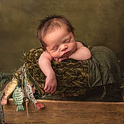 Houston is registered to the contest to win money with this photo: baby, newborn, infant, sleeping, wooden_crate, blanket, plush, olive_green, arm, closed_eyes, portrait, studio_lighting, prop, peaceful, cozy, hand, textured_background, painted_fish, wood, soft_fabric