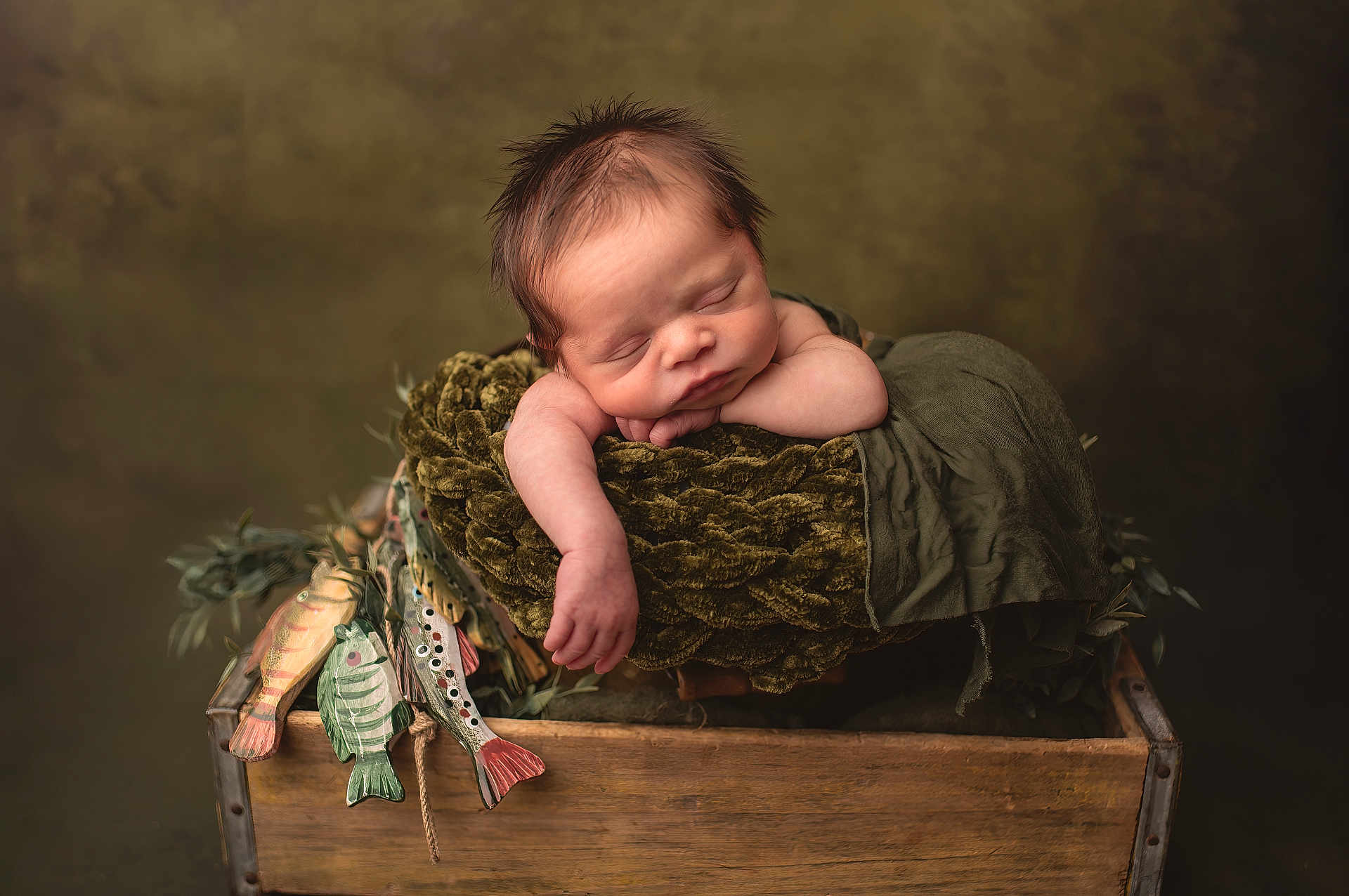 Houston is registered to the contest to win money with this photo: baby, newborn, infant, sleeping, wooden_crate, blanket, plush, olive_green, arm, closed_eyes, portrait, studio_lighting, prop, peaceful, cozy, hand, textured_background, painted_fish, wood, soft_fabric