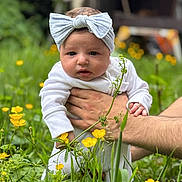 Diana is registered to the contest to win money with this photo: baby, child, headband, white_clothing, hand, flower, yellow_flower, greenery, outdoor, nature, grass, person, infant, cute, portrait, garden, flora, young, holding, skin