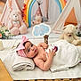 Diana joined the competition — help win amazing prizes! baby, infant, towel, pink_bow, headband, teddy_bear, rainbow, plush_toy, wooden_floor, blanket, cute, child, indoor, soft_lighting, portrait, laying_down, nursery, decor, toy, curious