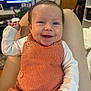 Novalee is registered to the contest to win money with this photo: baby, smiling, infant, orange_clothing, corduroy, white_shirt, sitting, indoor, living_room, television, furniture, plant, person, happy, cute, child, portrait, skin, hair, hand