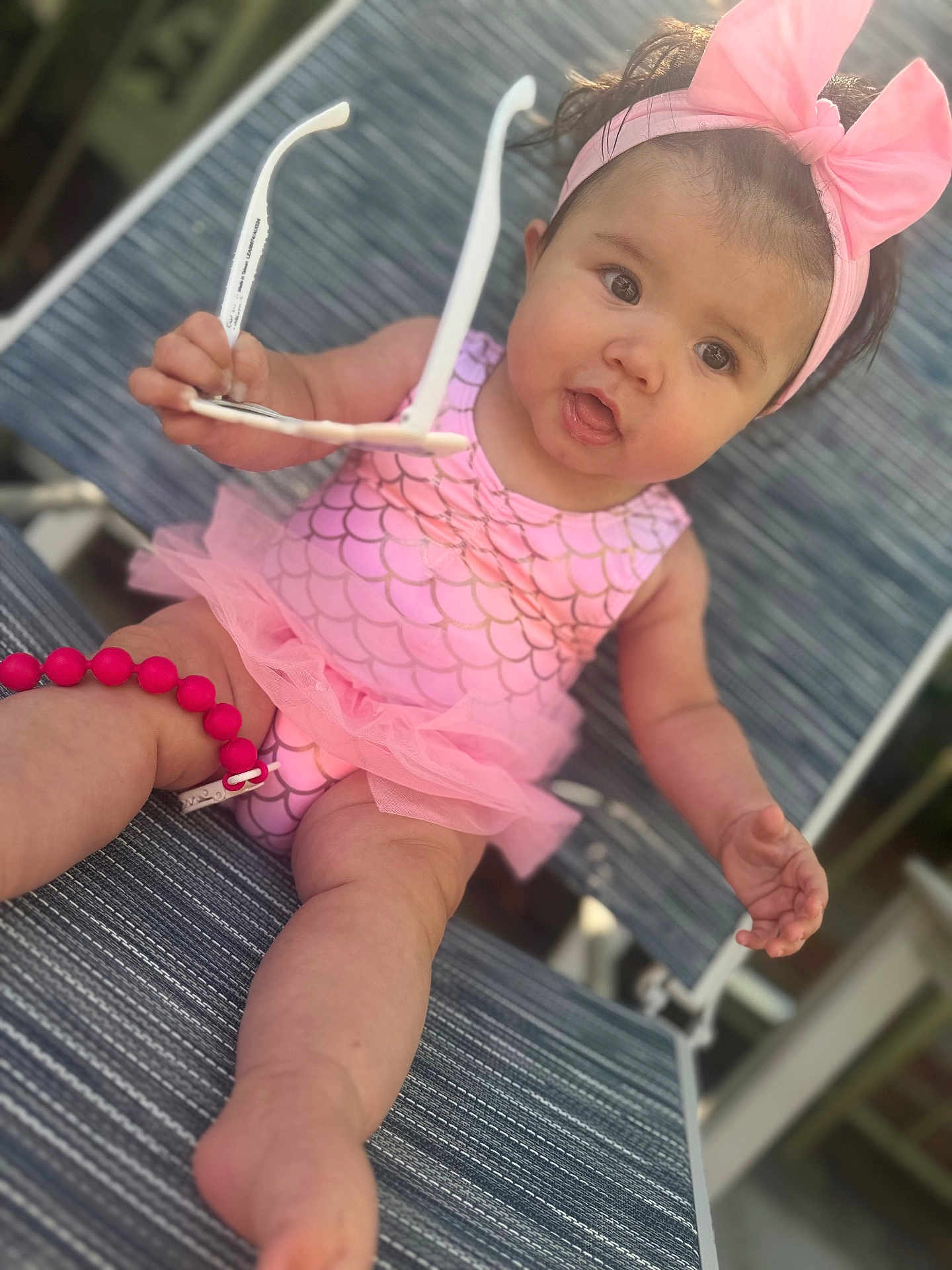 Princess Octavia joined the competition — help win amazing prizes! baby, child, pink_bow, headband, sunglasses, swimsuit, mermaid_pattern, tutu, lounge_chair, outdoor, summer, cute, curious, infant, person, sitting, legs, arm, face, expression