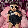 Princess Octavia is registered to the contest to win money with this photo: baby, child, sunglasses, heart_shaped, black_dress, pink_chair, confetti, party, indoor, portrait, cute, fashion, accessory, sock, furniture, decor, celebration, fun, happy, person