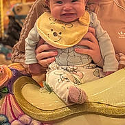 Princess Octavia is registered to the contest to win money with this photo: baby, child, person, smile, bow, bib, clothing, hand, carousel, horse, flower, colorful, toy, amusement_park, happy, fun, indoor, jacket, adidas, portrait