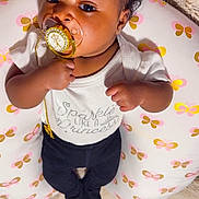 Kalexi is registered to the contest to win money with this photo: baby, pacifier, pillow, butterfly_pattern, blanket, clothing, infant, cute, lying_down, indoors, face, person, child, soft_texture, decor, black_hair, white_shirt, dark_pants, closeup, pacifier_clip