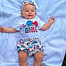 baby, child, smiling, headband, white_blanket, outdoor, grass, clothing, toddler, cute, summer, happy, person, portrait, infant, patterned_clothes, lying_down, celebration, festive, american_flag