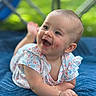 Omie is registered to the contest to win money with this photo: baby, child, smiling, happy, blue_quilt, floral_outfit, teething_toy, outdoor, green_background, portrait, cute, infant, face, skin, eyes, mouth_open, hand, lying_down, soft_light, closeup