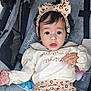 baby, child, toddler, infant, stroller, headband, bow, clothing, leopard_print, cute, person, face, eyes, hand, soft_lighting, indoor, expression, fabric, seat, baby_gear