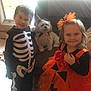 Ms Bella joined the competition — help win amazing prizes! child, children, dog, costume, halloween, skeleton, pumpkin, orange, black, smile, indoors, window, chair, pet, cute, happy, tulle, ribbon, flower, small_dog