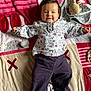 baby, child, smiling, lying_down, blanket, plush_toy, pacifier, colorful, patterned_clothing, indoor, floor, cute, happy, infant, soft_toy, person, casual_clothing, head, face, playtime