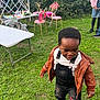toddler, child, grass, outdoor, jacket, overalls, shoes, chairs, tables, people, greenery, casual_clothing, daylight, curious, walking, playful, backyard, pink_chairs, white_table, social_gathering