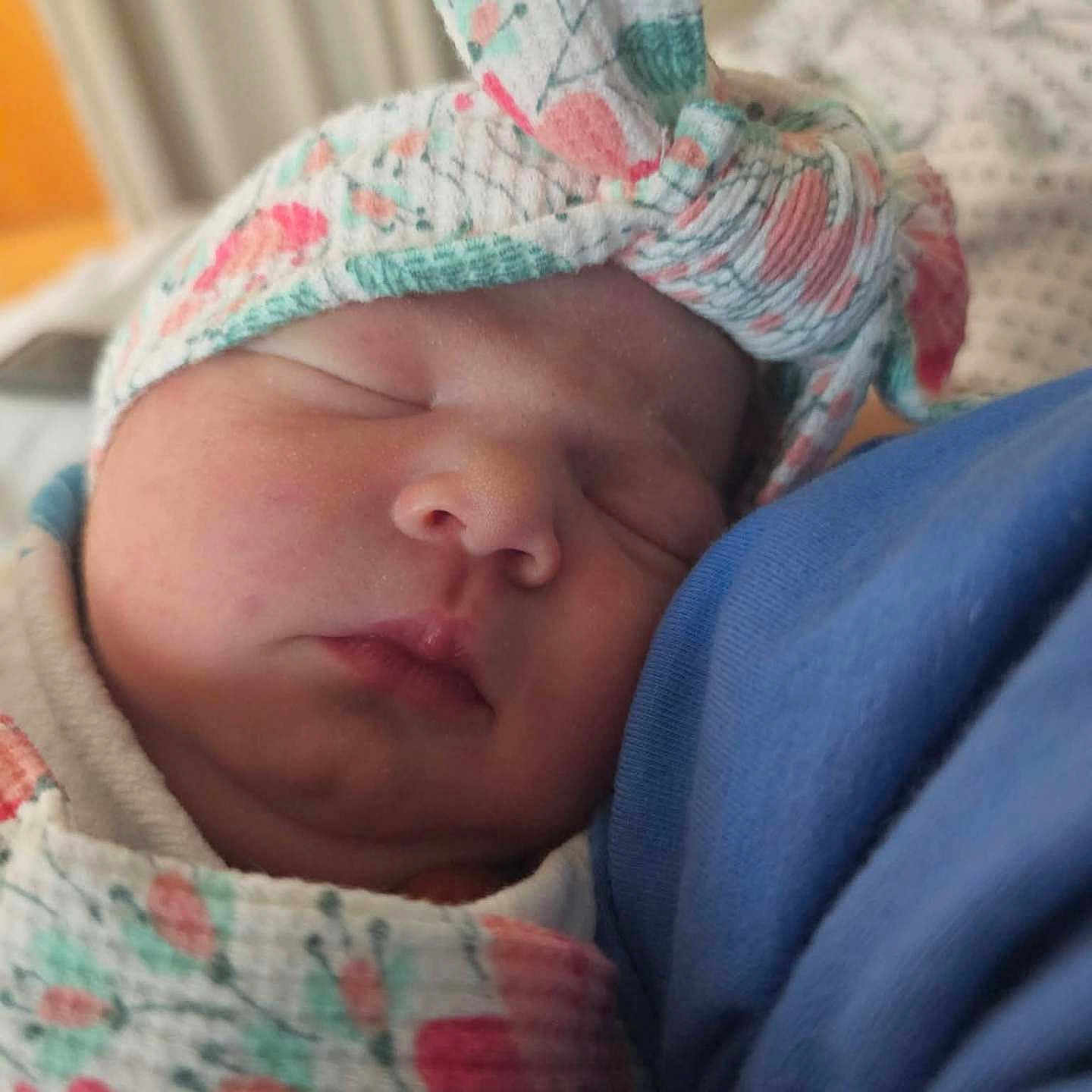 Lilly is registered to the contest to win money with this photo: newborn, baby, sleeping, infant, portrait, close_up, swaddled, blanket, hat, floral, peaceful, cozy, face, eyes_closed, nose, mouth, skin, blue_clothing, indoor, candid