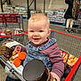 Logan joined the competition — help win amazing prizes! baby, child, shopping_cart, warehouse_store, grocery, toy, plush_toy, smiling, denim_overalls, striped_shirt, person, shopping, retail, indoor, happy, infant, food, background_person, store_shelves, packaged_goods