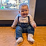 baby, background, casual_clothing, child, cute, face, happy, indoor, infant, jeans, natural_light, person, portrait, sitting, smiling, sock, suspenders, white_shirt, window, wooden_surface
