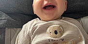 Logan is registered to the contest to win money with this photo: baby, smiling, infant, onesie, striped_clothing, koala_patch, happy, cute, lying_down, indoors, child, portrait, soft_surface, closeup, cheerful, young_child, casual_clothing, fabric, adorable, face
