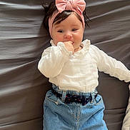 Catalia participe au concours pour gagner de l'argent avec cette photo : baby, bed, bedding, belt, bow, child, cute, gray_sheet, hair, hand_in_mouth, headband, indoors, infant, jeans, lying_down, portrait, smile, socks, white_blouse, wooden_floor
