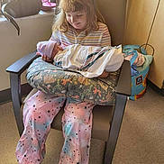 Julianne is registered to the contest to win money with this photo: child, baby, newborn, hospital, chair, pillow, blanket, clothing, person, smile, happy, indoor, floor, bag, window, footwear, hair, holding, striped_shirt, casual_wear