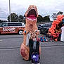child, costume, inflatable, t_rex, dinosaur, outdoor, parking_lot, halloween, pumpkins, balloons, kids, smile, candy_bucket, event, vehicle, trees, cloudy_sky, people, festive, celebration